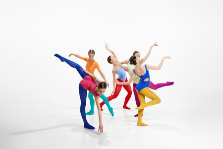 Group of artistic female ballet dancers in bright, multicolored clothes performing, dancing against grey studio backgroundの写真素材
