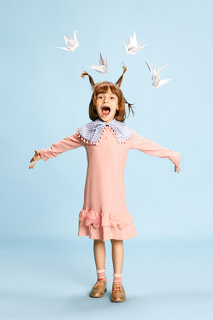 Full-length portrait of happy little girl, child in pink dress posing against blue studio background. Fantasy and fairytalesの写真素材