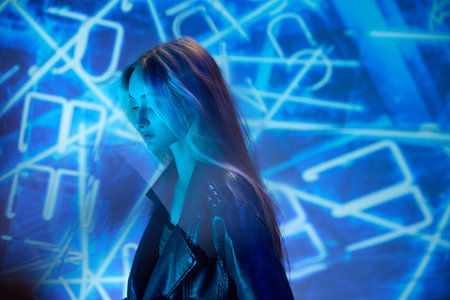 Thoughtful look. Portrait of young beautiful girl in leather jacket posing over blue background with...