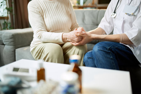 Doctor giving support and hope to her elderly female patient. Woman holding hand of senior lady at homeの写真素材