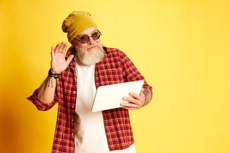 Portrait of stylish bearded mature man in casual clothes, shirt, sunglasses and hat, talking on...