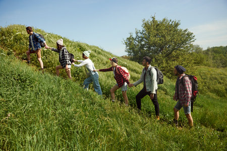 Group of young people, friends walking up the hill on warm spring day. Men and women going hiking,...