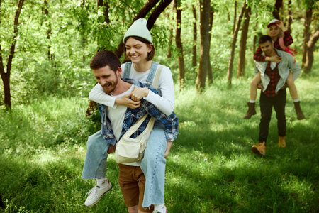Two young couple, men and women walking in forest, going hiking on warm sunny day. Girls sitting on...