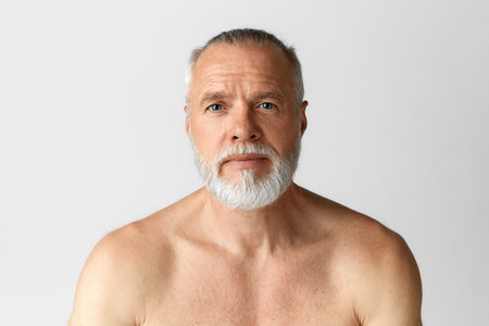 Portrait of handsome middle-aged man with blue eyes posing shirtless, looking at camera against grey backgroundの写真素材