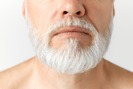 Cropped close-up image of grey-haired mans beard. Taking care after hair and beard. Mature male model against grey backgroundの写真素材