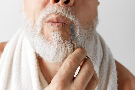 Cropped image of mature mans face, male model taking care after face, cutting moustaches against grey backgroundの写真素材