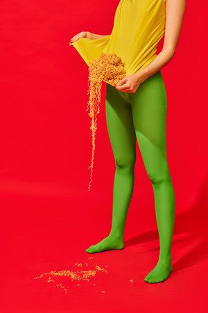 Cropped image of female legs in green tights and yellow t-shirt with noodles inside against vivid red backgroundの写真素材