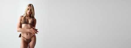 Portrait of attractive young girl with blonde hair, skin tanned body posing in swimsuit against grey studio backgroundの写真素材