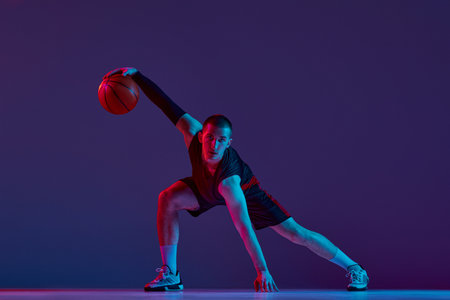 Concentration and motivation. Young man, basketball player in motion with ball against purple studio background in neon light.の写真素材