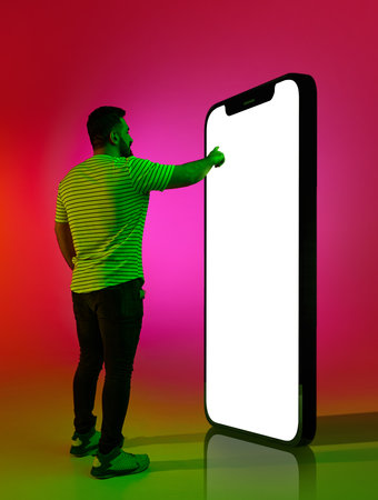 Full-length image of man in casual clothes touching screen of giant 3D model of phone against...
