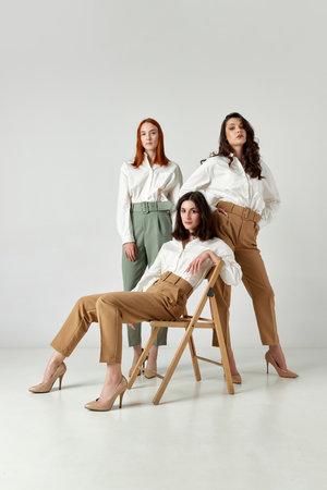 Portrait of elegant, stylish, attractive young women in official clothes posing against light studio backgroundの写真素材