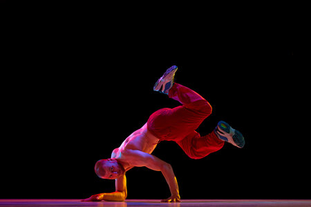 Muscular, shirtless, young man dancing hip-hop, breakdance against black studio background. Modern performanceの写真素材