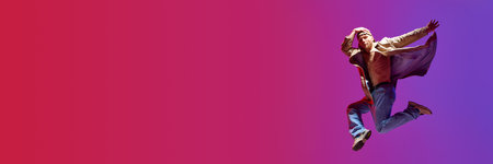Talented, artistic man in stylish clothes dancing breakdance against pink purple studio background