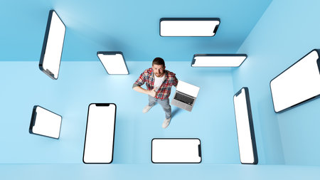 Conceptual design. Man with 3d mobile phone screens over blue background holding laptop. Online...