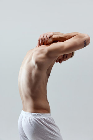 Strong, muscular, relief male back. Healthy body. Young man posing in underwear against grey studio backgroundの写真素材
