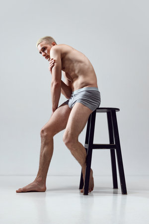 Handsome, young man with fit, relief, strong, muscular body posing shirtless in underwear against grey studio backgroundの写真素材