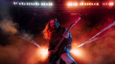 Rock and roll concert. Artistic, expressive man with long hair playing guitar and making performance, emotionally singingの写真素材