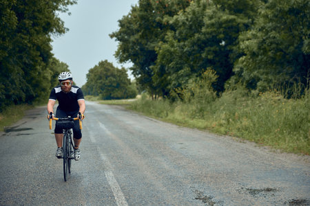 Young bearded man, cyclist in helmet, glasses and uniform riding bike on wet road in cloudy chill evening. Forest rideの写真素材