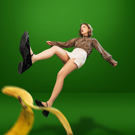 Creative image with young girl in stylish, animal print blouse and white shorts slipping on banana peel and falling downの写真素材
