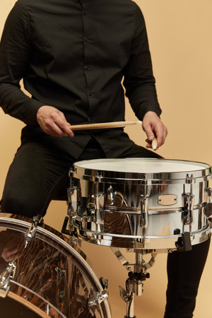 Cropped image of stylish man in black clothes. Close-up of male hands playing drums against studio backgroundの写真素材