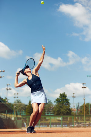 Full-length dynamic image of young athletic woman, tennis player in uniform during game, playing at open air stadium, court on warm dayの写真素材