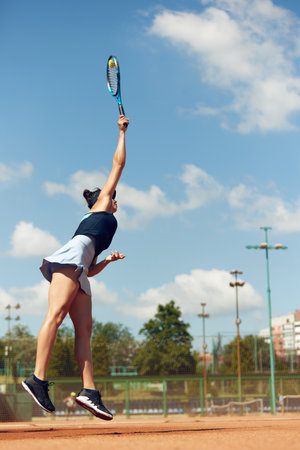 Concentrated female tennis player in motion during game, raining, playing tennis at open air court on sunny dayの写真素材