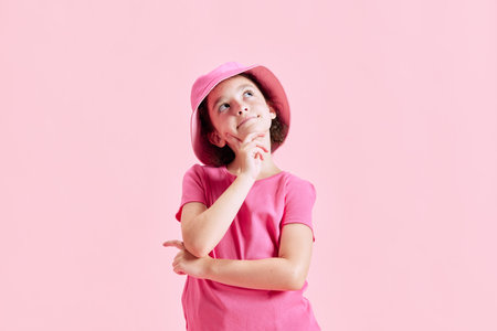 Portrait of cute little girl, child in panama standing with dreaming face against pink studio backgroundの写真素材
