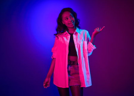 Portrait of young attractive african woman in white shirt posing with dreaming face against gradient...