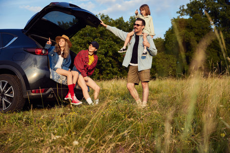 Young happy man and woman, parents spending time together with children, going hiking driving to forest. Warm summer day activityの写真素材