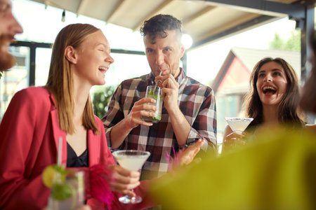 Joyful young people, men and women, friends meeting at cafe, drinking cocktails, talking, having...