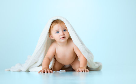 Cute, adorable baby, child in calmly in towel starting crawling against light blue studio background