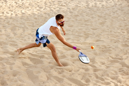 Dynamic image of young man playing beach tennis, hitting ball with racket. Outdoor training on warm summer day. Top viewの写真素材