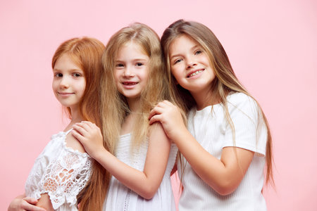 Beautiful little girls, sisters, children posing with smile against pink studio background