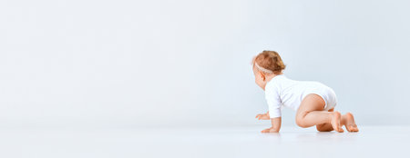 Beautiful little girl, toddler in comfortable clothes crawling against grey studio background. Curious, playful kidの写真素材