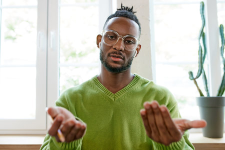 Young african man in glasses sitting at home, working studying. Online video call. Man lively...