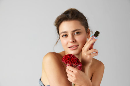 Portrait of young beautiful woman with nude makeup, using lip oil against grey studio backgroundの写真素材