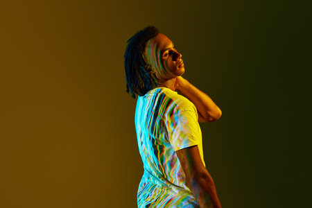 Side view portrait of young african man with colorful digital reflection on body standing over gradient green background in neon lightの写真素材