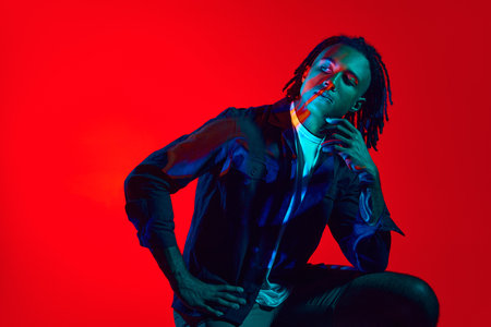 Young african man with neon filter reflection on face posing against red background in neon light. New visionの写真素材