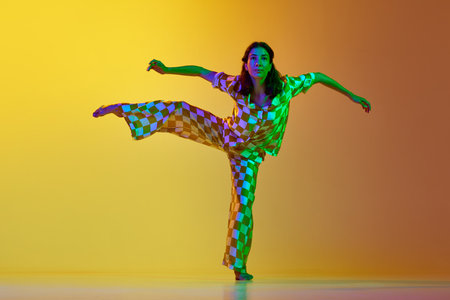 Young artistic, talented woman dancing contemporary, freestyle dance against gradient yellow orange background in neon lightの写真素材