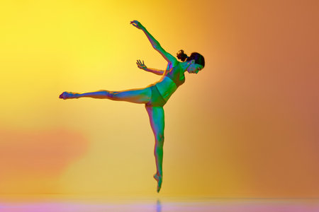 Young talented woman dancing contemp against gradient yellow orange background in neon light. Slim bodyの写真素材