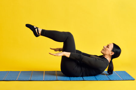 Endurance and strength. Sportive woman in black sportswear lying on fitness mat and doing press...