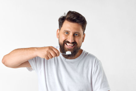 Perfect smile. Bearded mature man brushing teeth against white studio background. Dental hygieneの写真素材