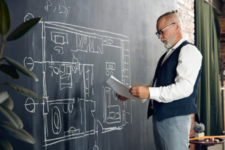 Stylish senior man, professional architect working with architectural design, making sketches on...