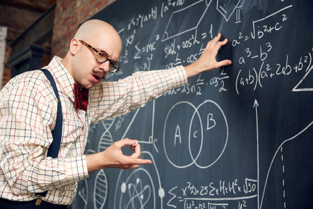 Young man, scientist standing at blackboard with formulas and calculations, thinking, counting in mind. Mathの写真素材