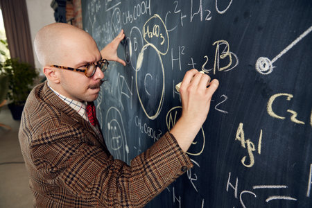 Young thoughtful man, scientist standing at blackboard with formulas and calculations, thinking, counting in mind. Chemistryの写真素材