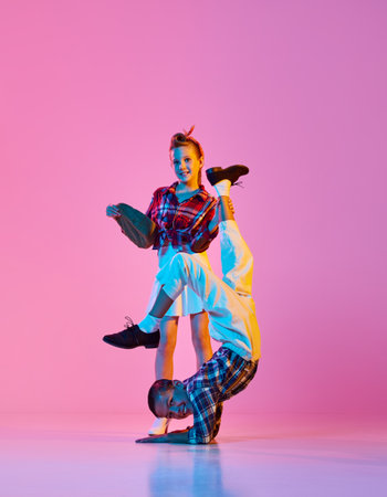 Flexibility. Stylish, active children, girl and boy in retro style clothes dancing against pink studio background in neon lightの写真素材