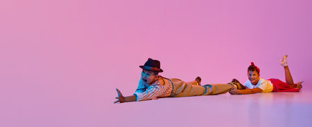 Emotional dance. Children, boy and girl in retro clothes performing against pink studio background in neon lightの写真素材