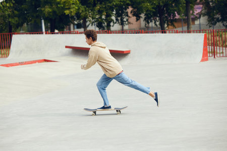 Teen boy in casual clothes skateboarding in skate park, outdoors, having fun with friendsの写真素材