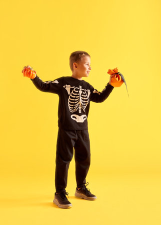 Trick or threat. Full-length of little boy, child in black costume, holding coin bag and pumpkin over yellow background. Halloweenの写真素材