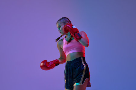 Teen athletic girl, MMA fighter in motion, training kicks against purple studio background in neon lightsの写真素材